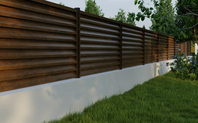 Wooden privacy fence with a white base and greenery in the background